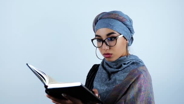 若い美しいアラビアのビジネスウーマンは、孤立した白い背景にペンを保持するノートに必要な情報を見つけた後、眼鏡に触れて驚きました — ストック動画