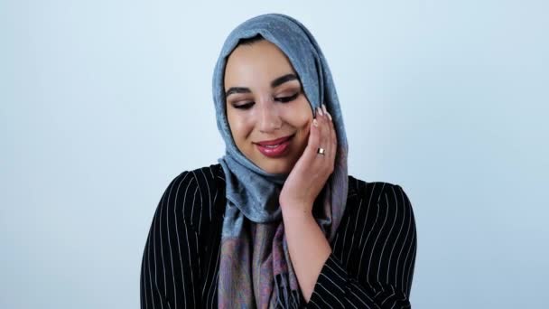 Молодая красивая арабская женщина улыбается, чувствуя себя немного застенчиво касаясь ее лица рукой на изолированном белом фоне — стоковое видео