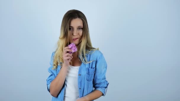 Jovem bela mulher mordendo um delicioso cupcake e torcendo outro cupcake em sua mão sobre fundo branco isolado — Vídeo de Stock