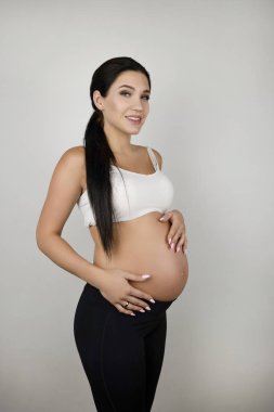 hamile esmer kadın izole beyaz arka plan üzerinde kadınsı görünümlü iki eliyle onu çıplak göbek tutarak
