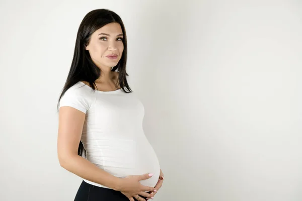 Beautiful pregnant brunette woman holding her pregnant belly with love and care on isolated white background — Stock Photo, Image