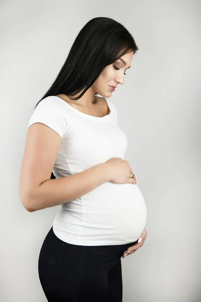 Mooie zwangere brunette vrouw houdt haar zwangere buik met liefde en tederheid op geïsoleerde witte achtergrond — Stockfoto