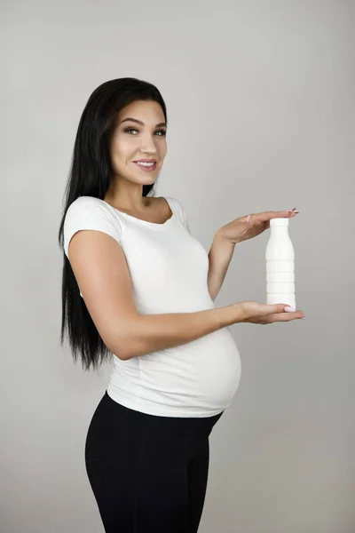Όμορφη έγκυος μελαχρινή γυναίκα κρατώντας μπουκάλι με κεφίρ γιαούρτι μεταξύ των χεριών της σε απομονωμένο λευκό φόντο — Φωτογραφία Αρχείου
