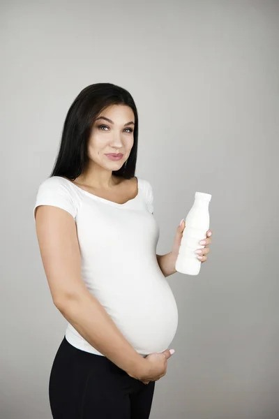 Beautiful pregnant brunette woman holding bottle with kefir smiling on isolated white background — Stock Photo, Image