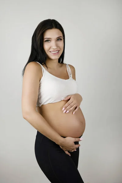 Bella donna bruna incinta che tiene la sua pancia nuda incinta cercando contenuto su sfondo bianco isolato — Foto Stock