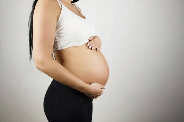 Zwangere brunette vrouw houdt haar naakte buik met beide handen op geïsoleerde witte achtergrond — Stockfoto