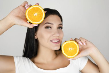 izole beyaz arka plan üzerinde onu güzel yüzünün yanında turuncu iki taze yarısı tutan genç esmer kadın