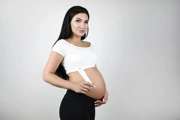 Zwangere brunette mooie vrouw houden lotion staande een halve beurt op geïsoleerde witte achtergrond — Stockfoto