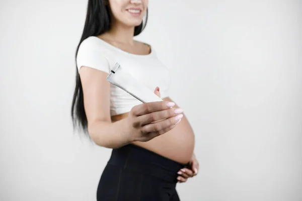 Těhotné bruneté ženy, držící krém na samostatné bílé pozadí — Stock fotografie