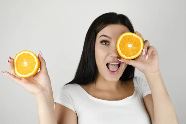 Młoda kobieta brunetka trzyma połowę pomarańczy w pobliżu jej pięknej twarzy i zamykając oko z drugą połową na białym tle białe — Zdjęcie stockowe