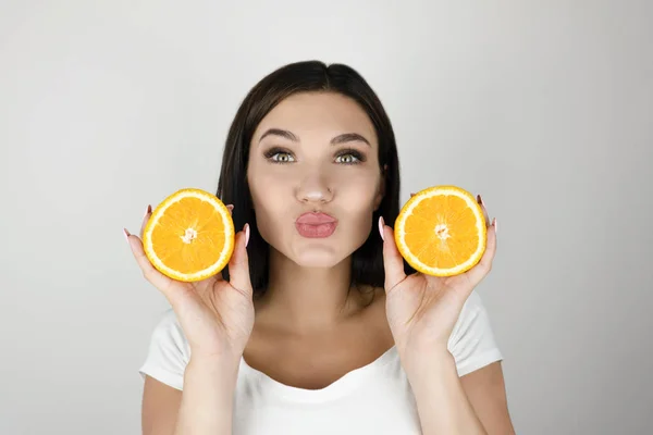 Młoda kobieta brunetka trzyma dwie połówki pomarańczy w pobliżu jej pięknej twarzy na białym tle biały — Zdjęcie stockowe