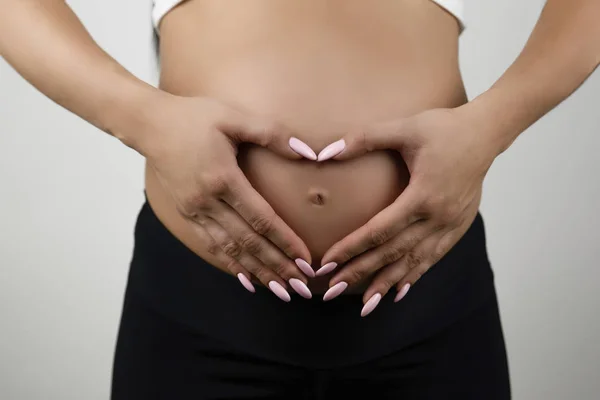 Pregnant woman showing heart sign with her hands on her naked pregnant belly isolated white background — Stock Photo, Image