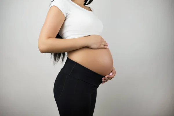 Brunette young woman holding her pregnant naked belly on isolated white background — Stock Photo, Image