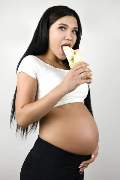 Брюнетка молодая беременная женщина ест шаурму на изолированном белом фоне — стоковое фото