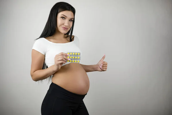 Bruneta mladá žena, která drží vitamíny v ruce ukazující jako nápis na izolovaném bílém pozadí — Stock fotografie