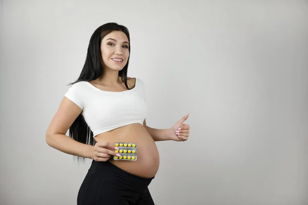 Bruna bella donna incinta che tiene le vitamine in mano mostrando come segno su sfondo bianco isolato — Foto Stock