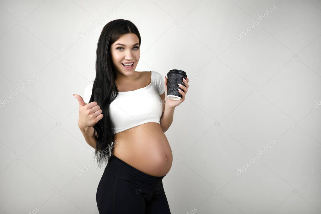 brunette young pregant woman with cup of coffee showing like sign on isolated white background