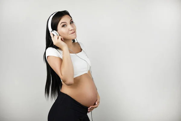 Brunette jong pregant vrouw luisteren haar favoriete artiest in koptelefoon op geïsoleerde witte achtergrond — Stockfoto