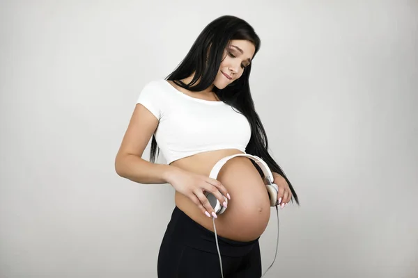 Bruneta Mladá krásná žena, která má u břicha sluchátka se sluchátky, se cítí šťastná na izolovaném bílém pozadí — Stock fotografie