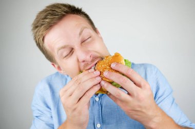 fast food restorandan taze lezzetli burger ısırma genç yakışıklı adam izole beyaz arka plan üzerinde yeme aç görünüyor