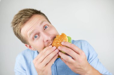 genç yakışıklı adam fast food restorandan taze lezzetli burger yiyor izole beyaz arka plan aç görünüyor