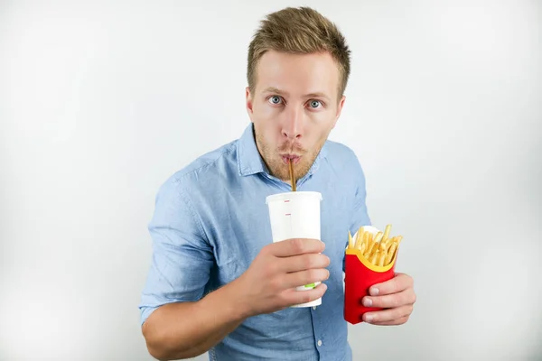 Bello giovane beve soda dalla tazza di papper e tiene patatine fritte dal ristorante fast food su sfondo bianco isolato — Foto Stock