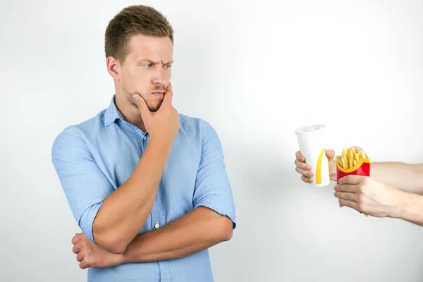 Jovem bonito homem pensa sobre ideia de comer fast food batatas fritas e beber refrigerante no fundo branco isolado — Fotografia de Stock