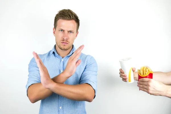 Ung, kjekk mann nekter å spise hurtigmat pommes frites og drikke brus og krysser armene uten tegn på isolert, hvit bakgrunn – stockfoto