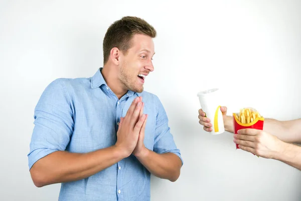 Young handsome man willing to eat fast food french fries and drink soda on isolated white background — Stock Photo, Image