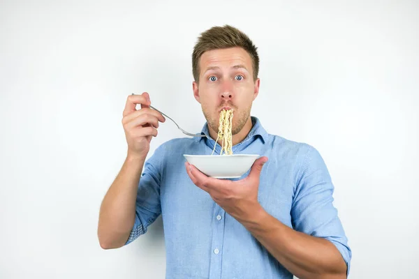 Jonge knappe man eten noedels op geïsoleerde witte achtergrond — Stockfoto