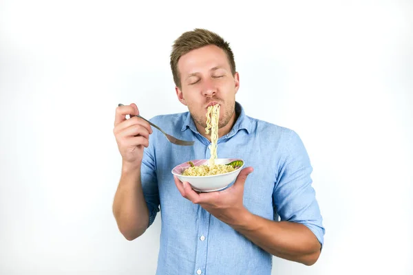 Jovem bonito homem comer macarrão parece com fome no isolado branco fundo — Fotografia de Stock