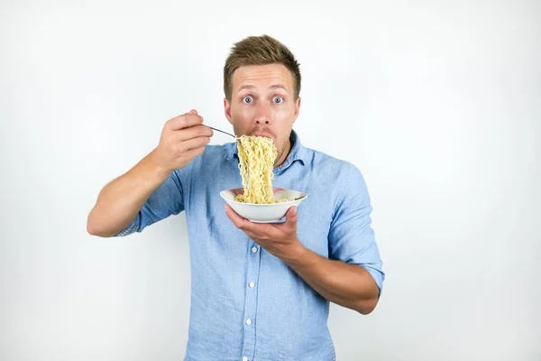 Young handsome man eating hot noodles looking hungry on isolated white background — Stock Photo, Image