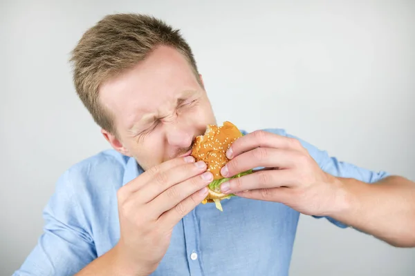 Anak muda makan burger segar lezat dari restoran cepat saji terlihat sangat lapar pada latar belakang putih terisolasi — Stok Foto