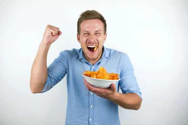 Giovane uomo biondo mangia fiches tenendo il pugno felicemente su isolato sfondo bianco — Foto Stock