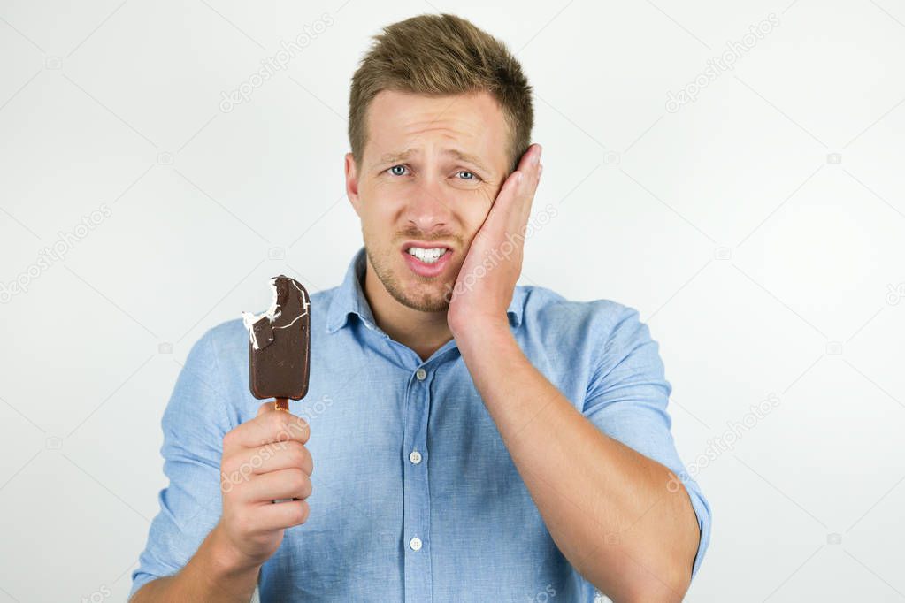 handsome young man just bit piece of cold chololate ice-cream and suffers toothache on isolated white background