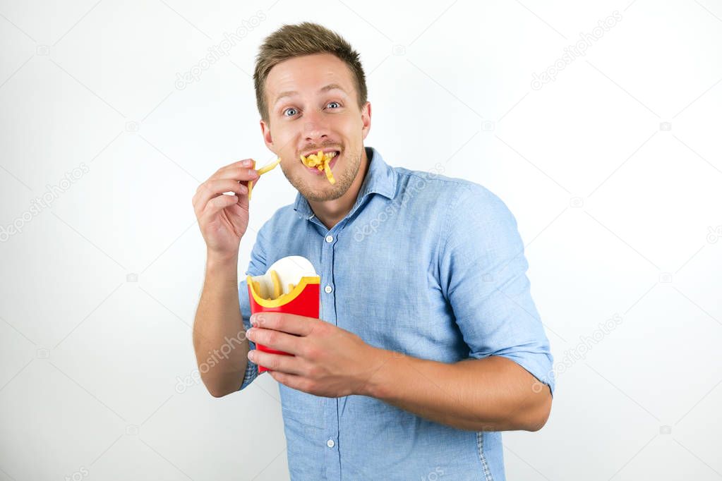 young handsome man eats french fries from fast food restaurant looks happy on isolated white background
