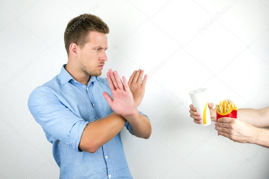 young handsome man refuses to eat fast food french fries and drink soda and crosses his arms like no sign on isolated white background