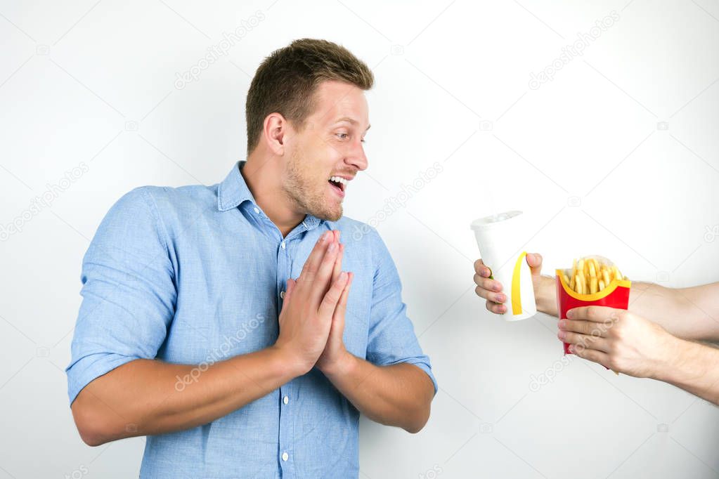 young handsome man willing to eat fast food french fries and drink soda on isolated white background