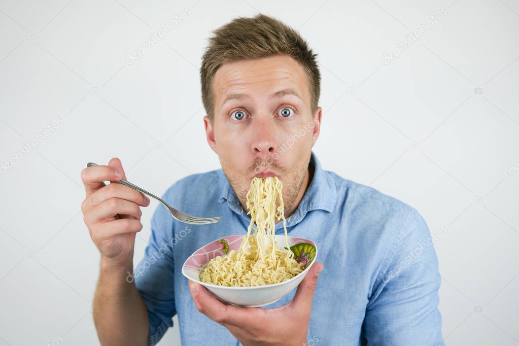 young handsome man with his eyes wide open eating noodles looking hungry on isolated white background
