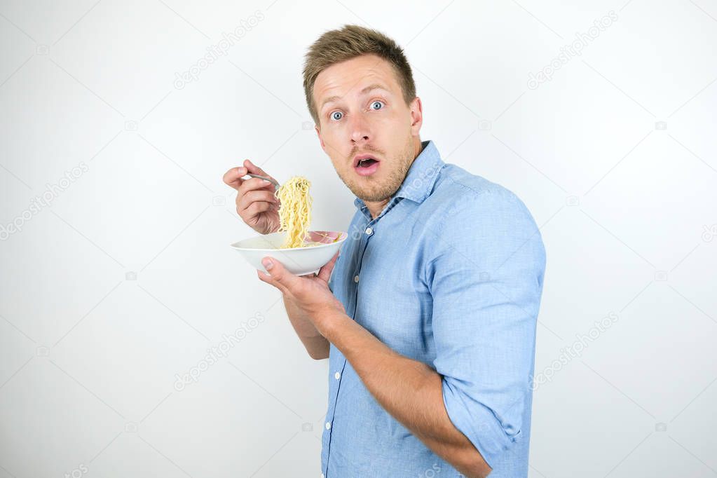 young handsome man eating hot noodles on the go looking hungry on isolated white background