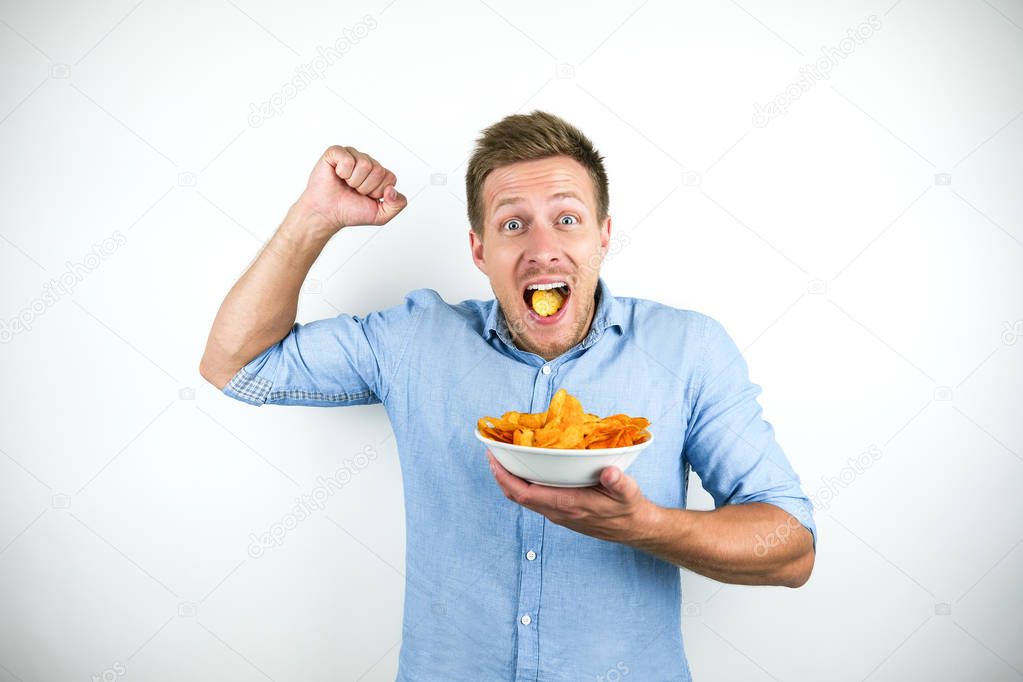 young handsome man eats chips holding his fist up happily on isolated white background
