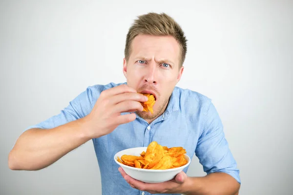 Young handsome man eats chips with paprika from plate looking hungry on isolated white background — Stock Photo, Image