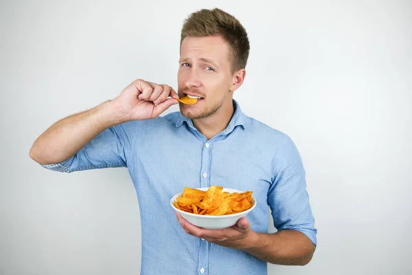 Jonge knappe man Holding plaat met chips putting chips met paprika in zijn mond op geïsoleerde witte achtergrond — Stockfoto