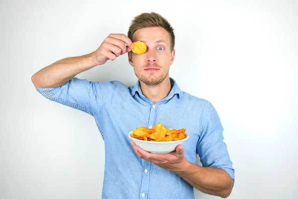 Jonge knappe man het houden van chips met papriknear zijn oog op geïsoleerde witte achtergrond — Stockfoto