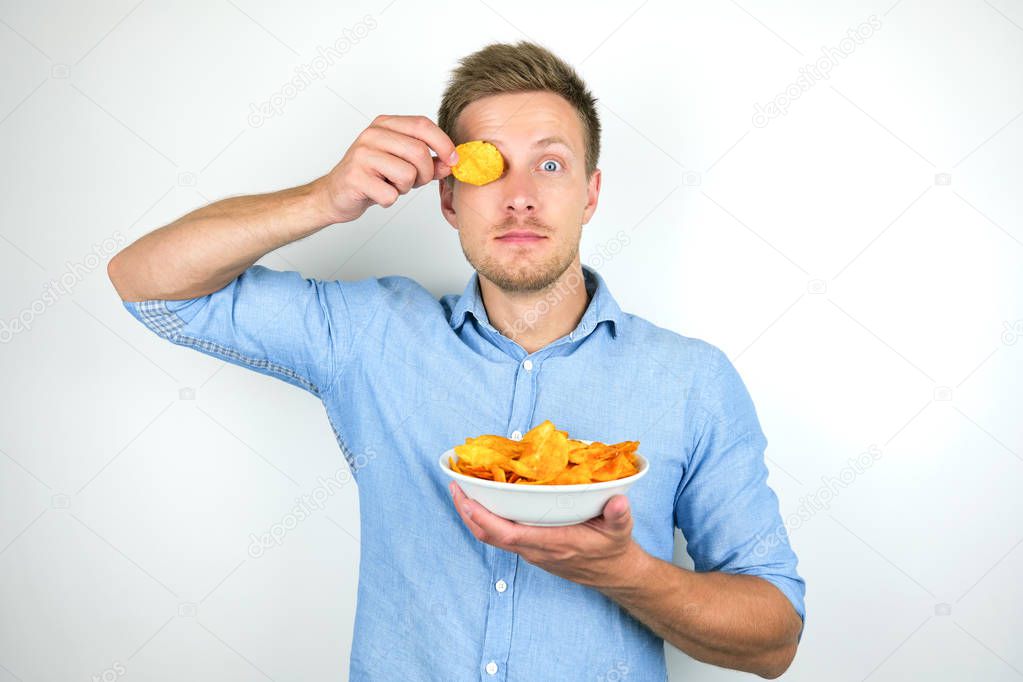 young handsome man holding chips with papriknear his eye on isolated white background