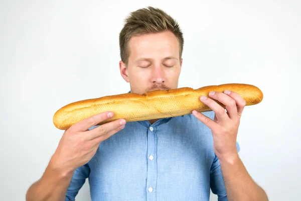 Jonge knappe man houdt ruikende hele Franse stokbrood op geïsoleerde witte achtergrond — Stockfoto