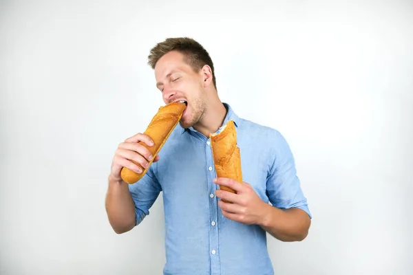 Jonge knappe man bijten helft van Frans stokbrood op geïsoleerde witte achtergrond — Stockfoto