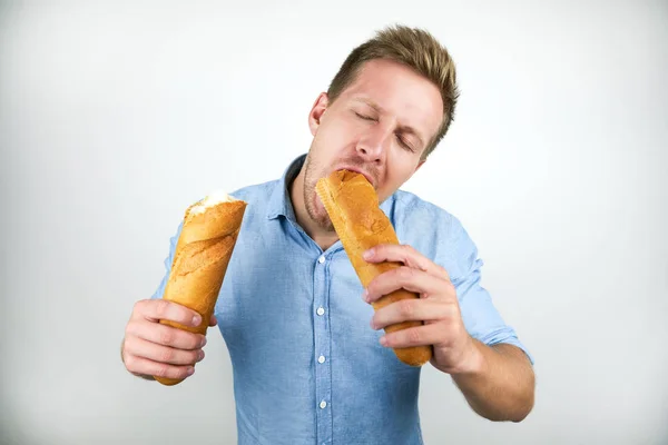 Pemuda tampan menggigit setengah baguette Perancis tampak lapar pada latar belakang putih terisolasi — Stok Foto