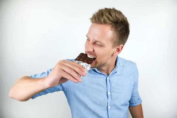 Jonge knappe man bijten chocolade bar gevoel hongerig op geïsoleerde witte achtergrond — Stockfoto