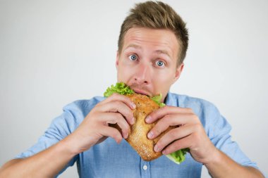 genç yakışıklı aç adam izole beyaz arka plan üzerinde iki eliyle tutarak salata yaprağı ile taze sandviç ısırma